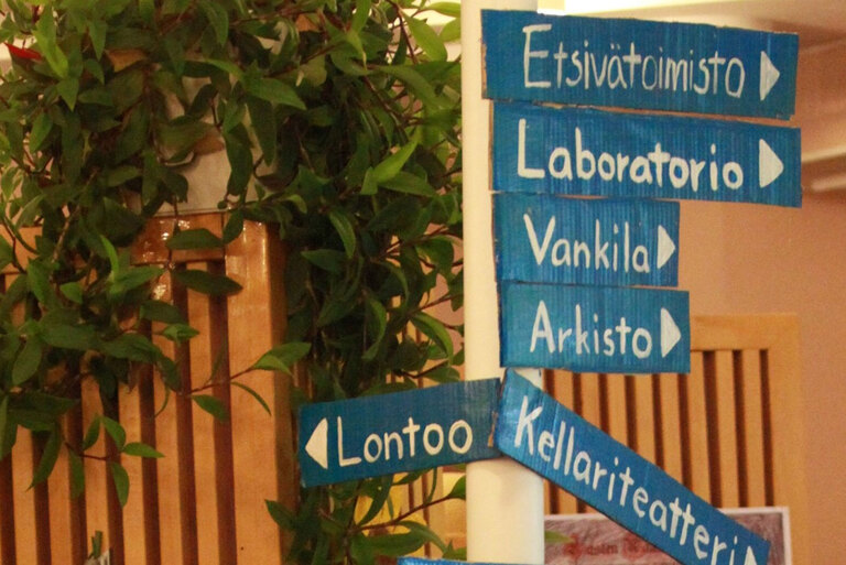 Pysstyssä olevassa opastinpylväässäov nuolikylti: Etsivätoimisto, Laboratorio, Vankila, Arkisto, Lontoo ja Kellariteatteri.