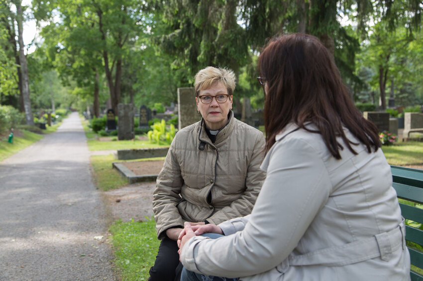Pastori ja sureva nainen ovat istahtaneet Kalevankankaan hautausmaan penkille puhumaan.