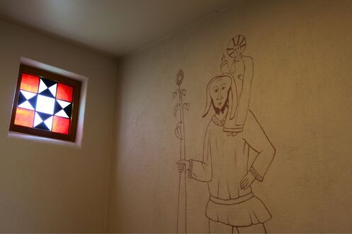 Yksinkertainen viivapiirros Pyhästä Kristoforoksesta ja Jeesus-lapsesta koristaa kappelin seinää, vierellään värikäs, tähtimäinen lasimaalausikkuna, joka valaisee tilaa.