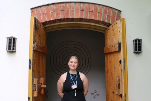 Nuori vaaleahiuksinen nainen hymyilee kappelin ovella.