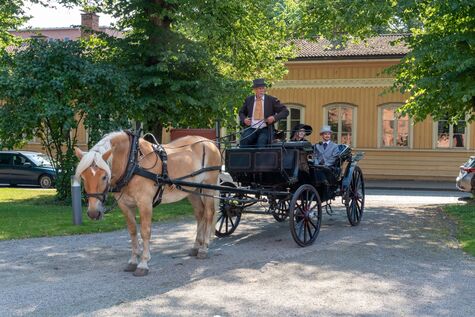 1800-luvun vaatteisiin pukeutunut kaksikko hevosvankkureiden kyydissä.