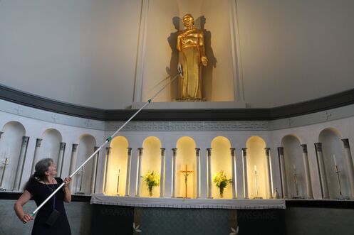 Naispuolinen suntio pyyhkii pitkällä siivousvarrella pölyjä Viinikan kirkon Kristus-veistoksesta.
