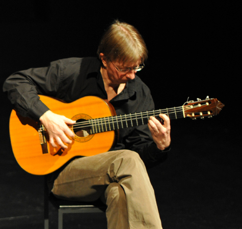 Janne Lehtinen soittaa kitaraa. Mies istuu keskittyneenä musiikkiin pimeässä konserttitilassa.