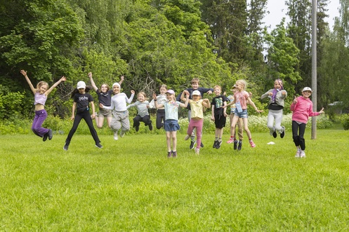 Kesäisen leirin lapsia hyppäämässä ilmaan nurmikolla.