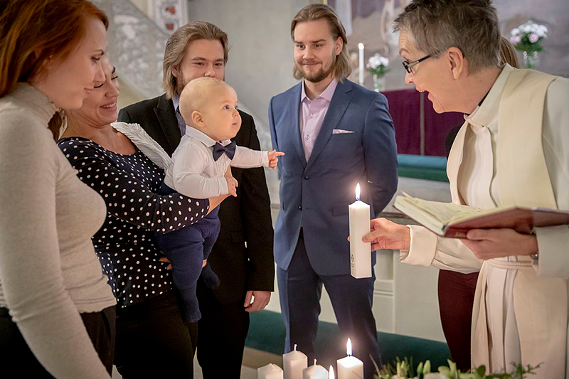 Aamukaste-tilaisuus. Pappi ilmeilee sylivauvalle.