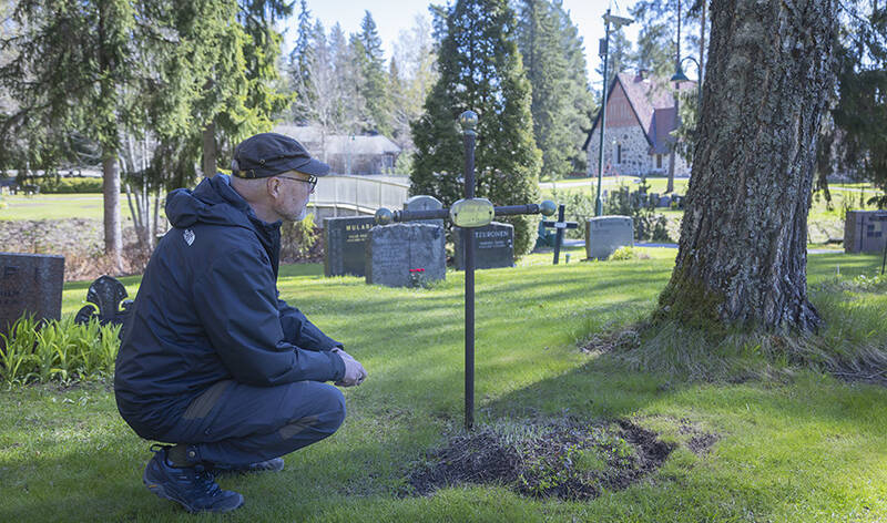 Henkilö katselee kyykkyasennossa hautaristiä keväisellä hautausmaalla.