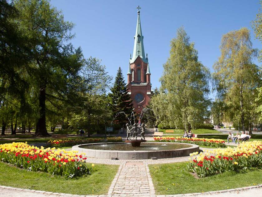 Pyynikin kirkkopuiston suihkulähde kevätpäivänä ja taustalla näkyy punatiilinen goottilainen kirkko.