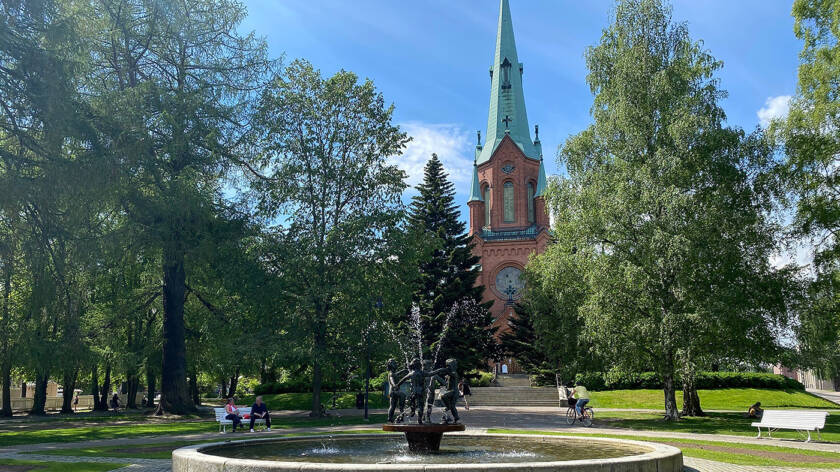 Pyynikin kirkkopuisto suihkulähde kesäpäivänä ja taustalla näkyy punatiilinen goottilainen kirkko.