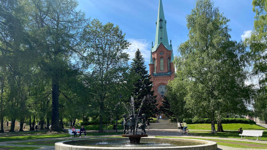 Pyynikin kirkkopuisto suihkulähde kesäpäivänä ja taustalla näkyy punatiilinen goottilainen kirkko.