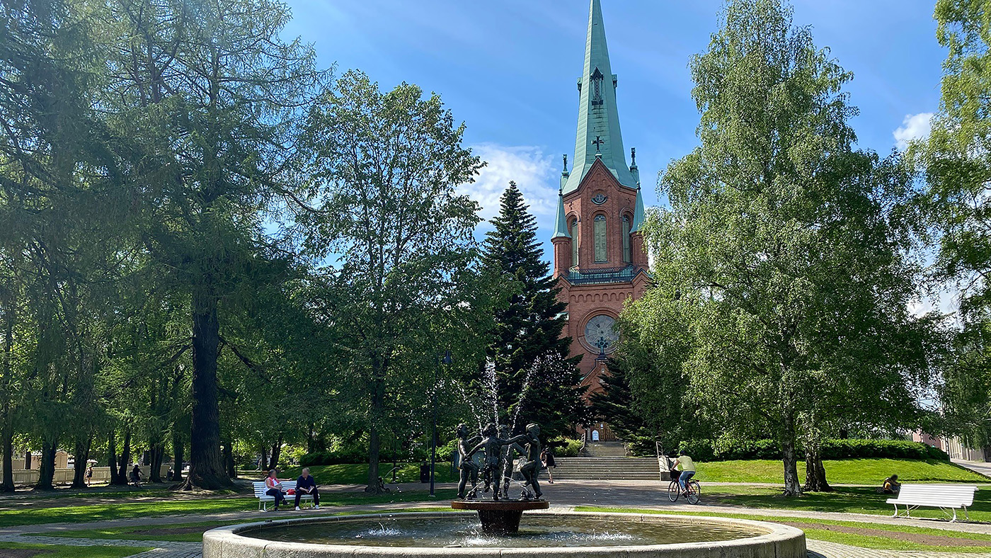 Pyynikin kirkkopuisto suihkulähde kesäpäivänä ja taustalla näkyy punatiilinen goottilainen kirkko.