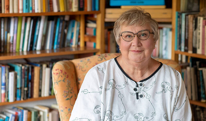 Anneli Kanto istuu kirjahyllyn edessä.