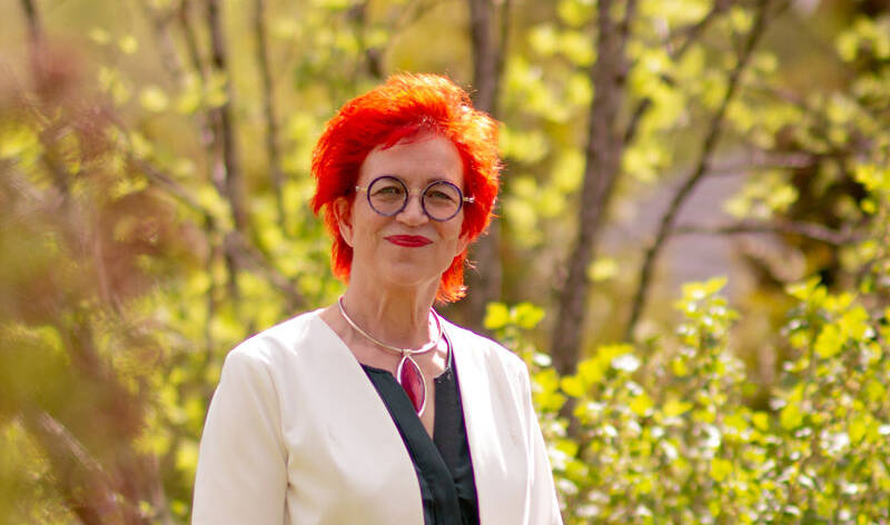 Eeva Mäkinen poseeraa hymyillen muotokuvaa varten metsässä.