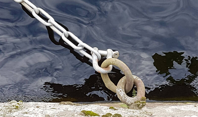 Veden päällä oleva metallinen ja hopeanvärinen ketju  on lukittu  koukkuun, joka on kiinni betonipinnassa.