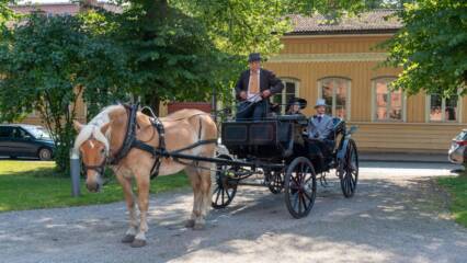 1800-luvun vaatteisiin pukeutunut kaksikko hevosvankkureiden kyydissä.