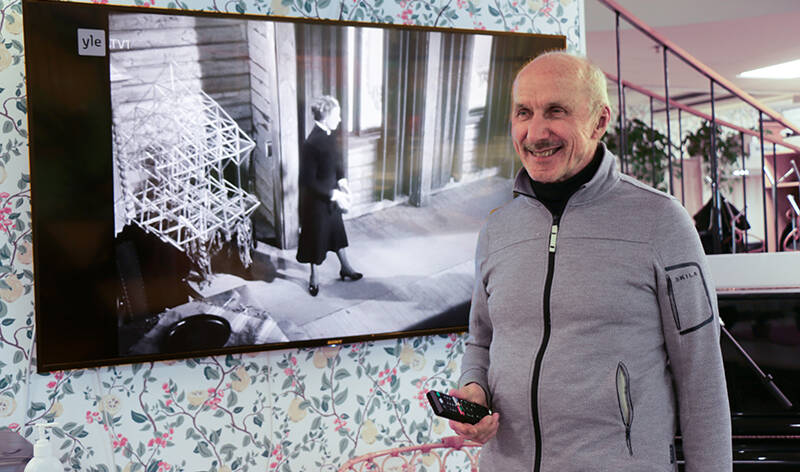 Henkilö kaukosäädin kädessä television vieressä.