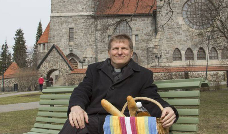 Olli Hallikainen istumassa penkillä Tampereen tuomiokirkon edustalla.