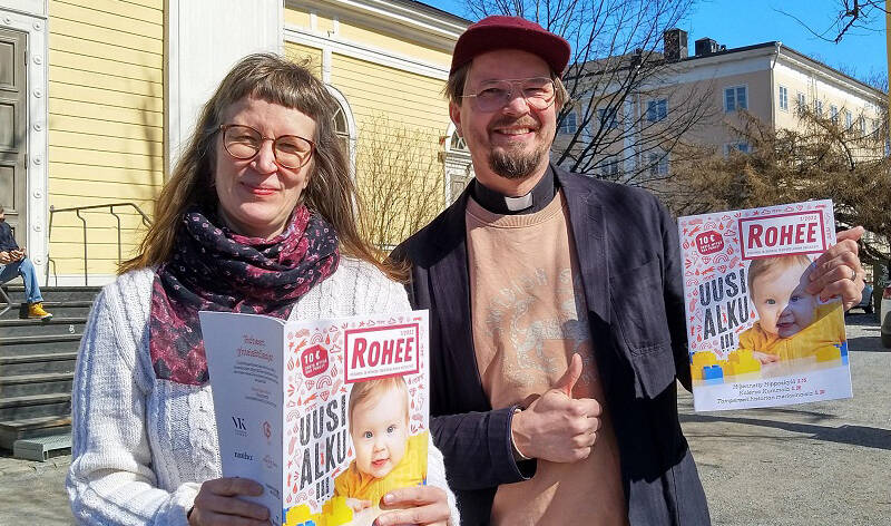 Hannele Huhtala ja Olli Viljakainen Vanhan kirkon edustalla pitävät käsissään Rohee-lehtiä.