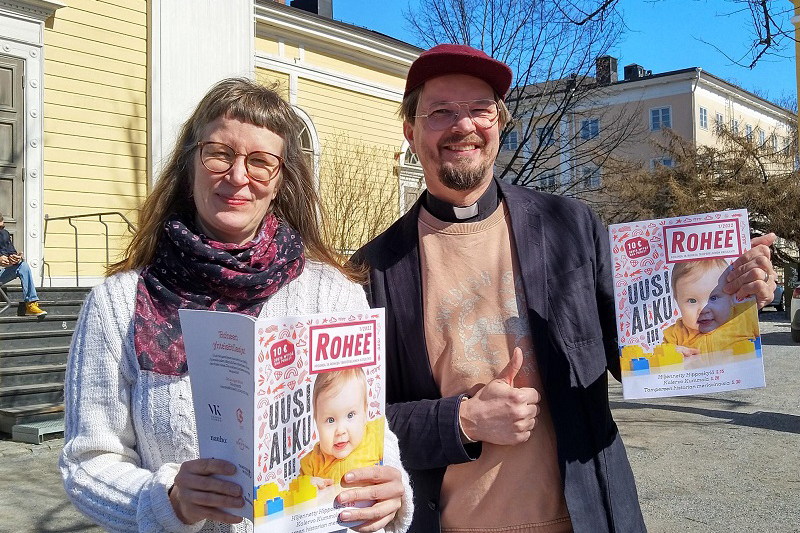 Hannele Huhtala ja Olli Viljakainen Vanhan kirkon edustalla pitävät käsissään Rohee-lehtiä.