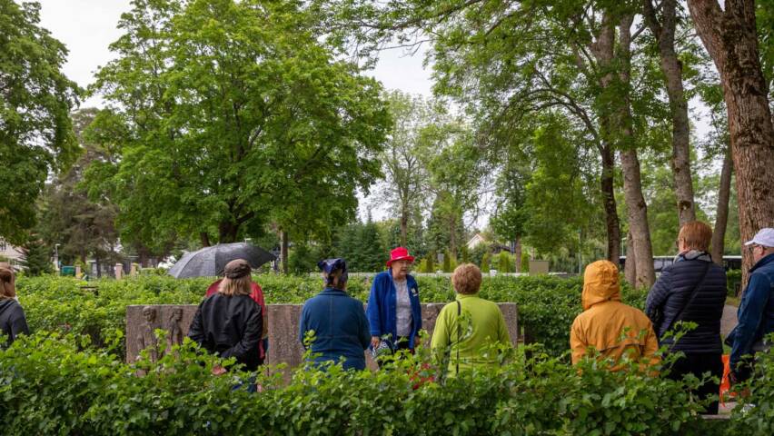 Hautausmaaopastukselle tulleet ihmiset kuuntelevat opasta haudan luona.