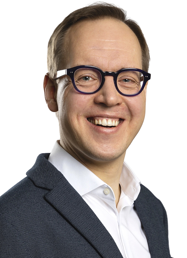 Ylävartalokuva nauravasta miehestä, jolla on pyöreät silmälasit.