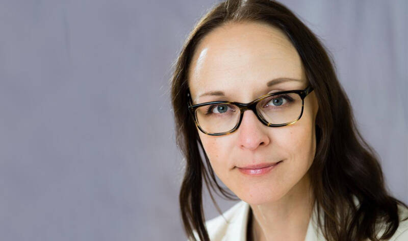 Kaupunkiteologi Henrietta Grönlund katsoo studiovalokuvassa katsojaa kohti. Taustalla on häivytetty harmaa kangas ja Grönlundin katse on kirkas.