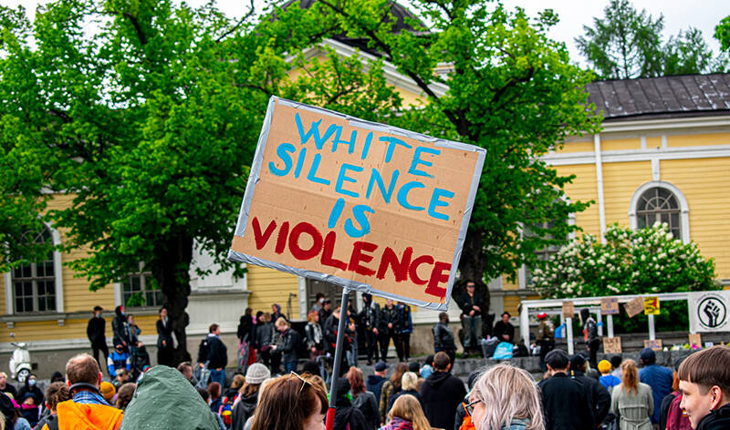 Suuri väkijoukko ulkona Tampereen keskustorilla. Väkijoukossa yhdellä on suuri kyltti, jossa lukee englanniksi: White silence is violence.