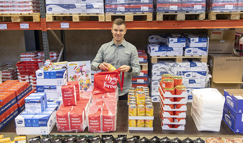 Janne Tamminen seisoo pöydän takana ja pakkaa ruokakassiin erilaisia ruokatuotteita.