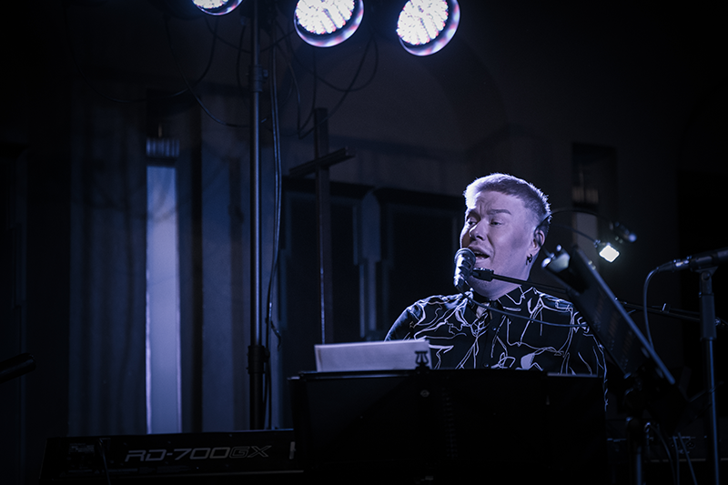 Mies laulaa ja soittaa pianoa hämärässä valaistuksessa.