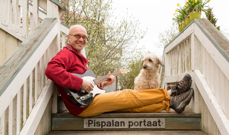 Mies istuu puisillaportailla, joissa lukee Pispalan portaat, kitara sylissä ja pieni koitra katselee vieressä.