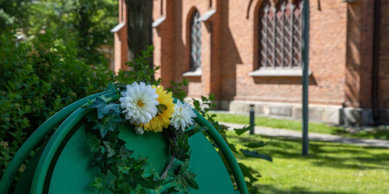 Kesäinen kuva Finlaysonin kirkolta. Kuvassa kyltti, kukkia ja taustalla näkyy Finlaysonin kirkko.
