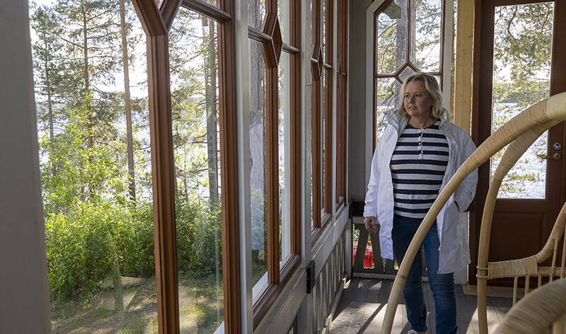 Nainen seisoo takki päällä lasiseinäisellä vanhalla kuistilla.