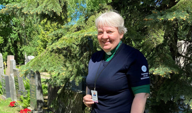 Hymyilevä nainen diakoniatyöntekijän virka-asussa Kalevankankaan hautausmaalla.