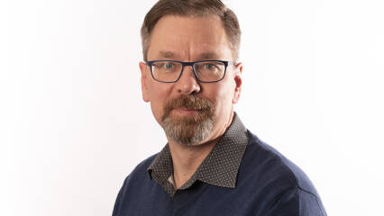 Henkilökuva parrakkaasta miehestä jolla silmälasit ja tummansineinen paita.