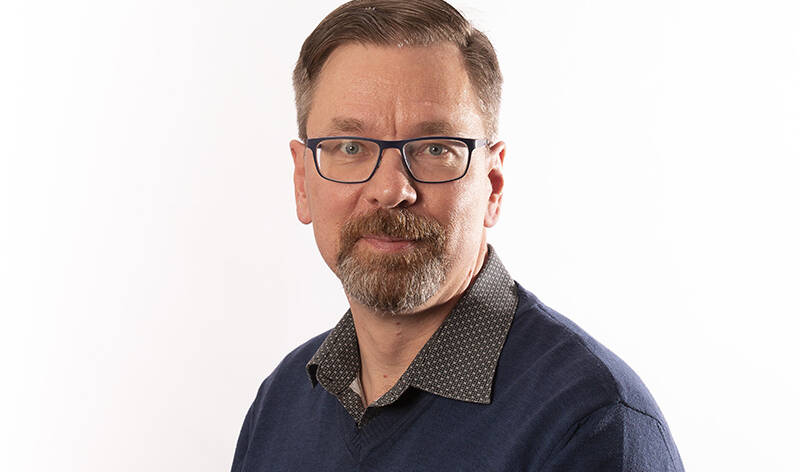 Henkilökuva parrakkaasta miehestä jolla silmälasit ja tummansineinen paita.