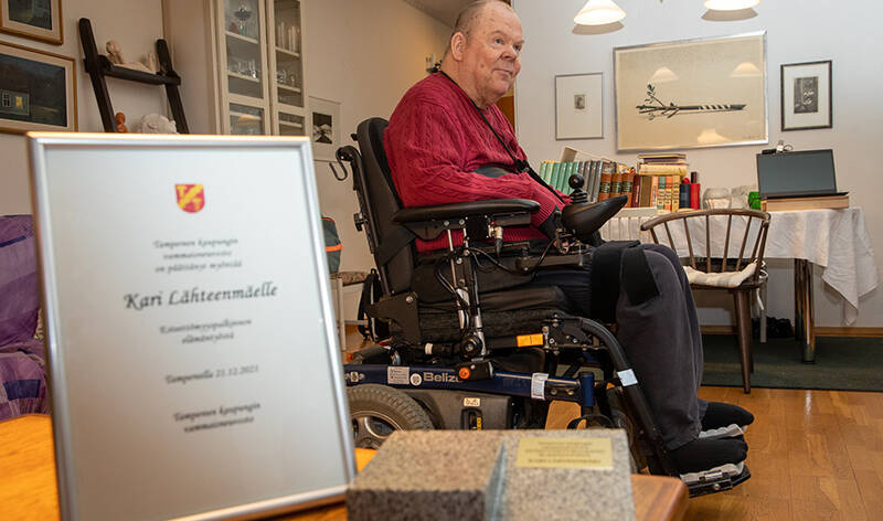 Etualalla kunniakirja, vähän kauempana mies sähköpyörätuolissa.