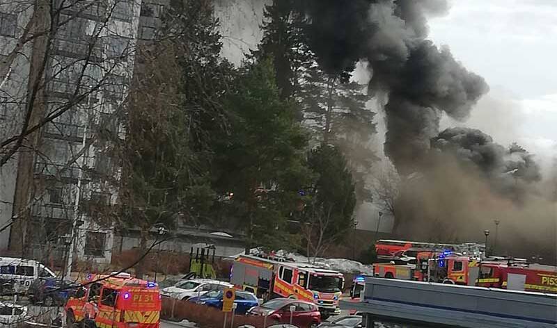 Etualalla ploautoja ja takana keroostalojen välissä näkyy tummaa savua, joka peittää maiseman.