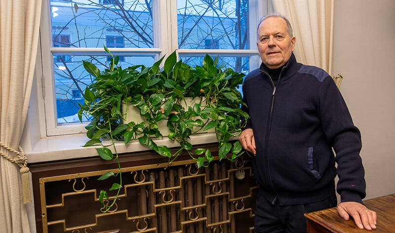 Sisäkuvassa mies nojaa käsivarrellaan ikkunaan, jolla on rehevä kasvi.