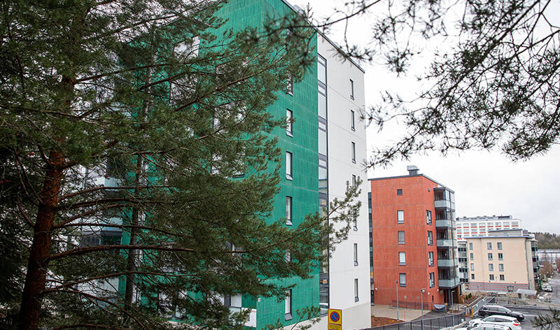 Monenvärisiä kerrostaloja oksien takaa alakulmasta kuvattuna.