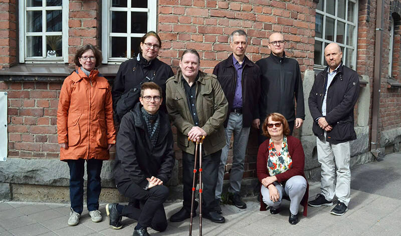 Kahdeksan henkilöä ulkovaatteissa tiilirakennuksen edessä.