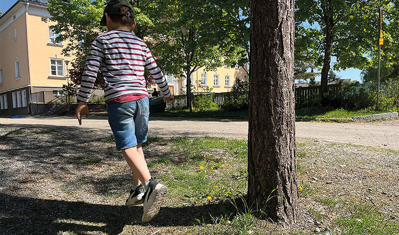 Lapsi selin kameraan ja ottaa hyppyaskeleen koulun edustalla.