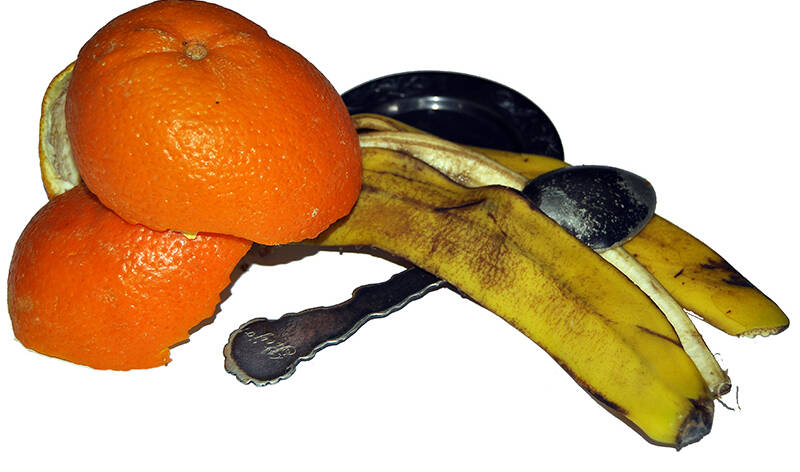Appelsiinin ja banaanin kuorten välissä on pieni lautanen ja tummunut lusikka.