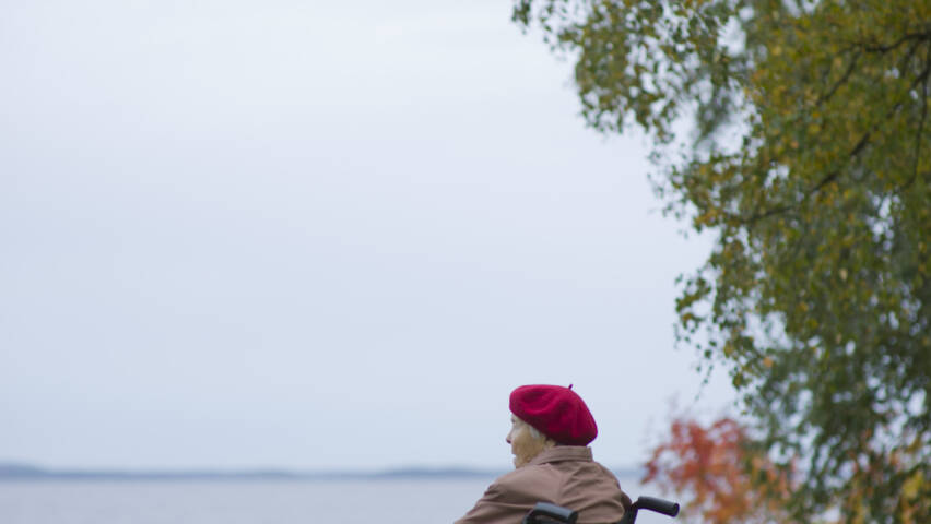 Vanhus pyörätuolissa katselee järveä syksyllä.