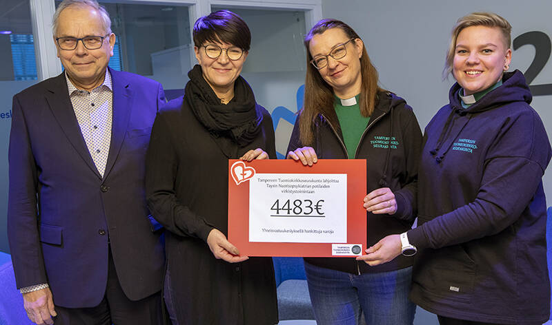 Neljä ihmistä seisoo rivissä. Kahdella keskimmäisellä on käsissään pahvi, jonka keskellä lukee 4483 €.
