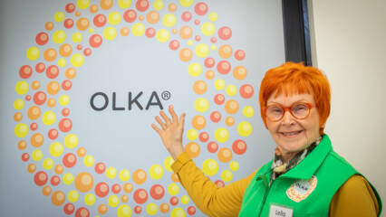 Nainen osoittaa pienistä palloista tehdyn ympyrän keskellä olevaa tekstiä OLKA.