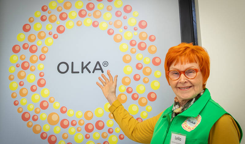 Nainen osoittaa pienistä palloista tehdyn ympyrän keskellä olevaa tekstiä OLKA.