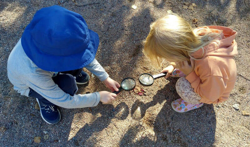 Kaksi lasta pihalla kyykistyneenä tutkimaan pihaa suurennuslasien kanssa.