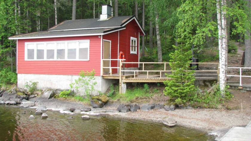 Punainen saunarakennus järveltä päon katsottuna on rannalla koivujen alla.