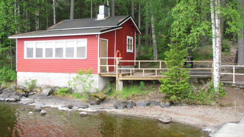 Punainen saunarakennus järveltä päon katsottuna on rannalla koivujen alla.