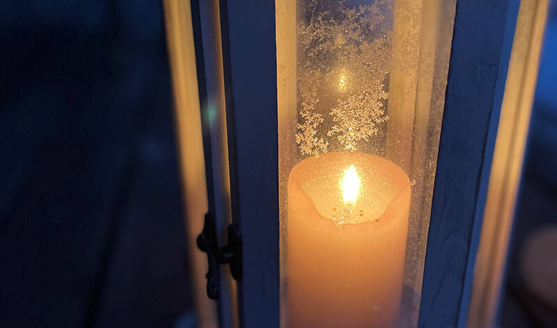 Kynttilä palaa lyhdyssä. Lyhdyn ikkunassa jäistä lumikidettä.