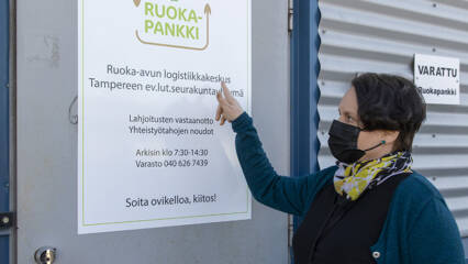 Nainen seisoo ruokapankin ovella ja osoittaa info-tekstejä.